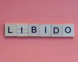 Słowa "LIBIDO" ułożone z klocków na różowym tle. Temat: spadek libido u mężczyzn po 30.