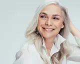 Lächelnde Frau mit silbernem Haar, die sich fragt, was ist Melanin, während sie ihre Hand durchs Haar fährt.