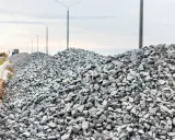 Ogromne hałdy kruszywa, gotowa mieszanka betonowa, czekają na budowie. W tle latarnie i niebo.