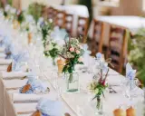 Disposition des couverts à la française sur une longue table dressée pour un événement, avec des fleurs sauvages et des serviettes à carreaux bleus.