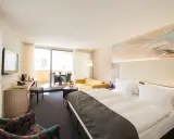 Modernes Hotelzimmer mit Doppelbett, Sofa, Schreibtisch und Balkon.