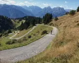 Radfahrer kämpft sich die Serpentinen des Monte Zoncolan hoch. Majestätische Berge im Hintergrund.