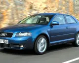 Niebieskie Audi A3 8P w ruchu, z widocznymi przednimi żarówkami, pędzi po drodze wśród skalistych zboczy.