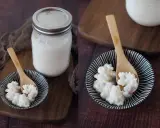 Kefir-Körner auf einem Löffel, bereit, Kefir selber zu machen. Daneben ein Glas mit fertigem Kefir.