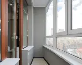 Wnętrze balkonu typu loggia z widokiem na miasto. Drewniane drzwi balkonowe i duże okna zapewniają dużo światła.