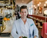 Uśmiechnięty menedżer firmy w jasnoniebieskiej marynarce siedzi przy barze w eleganckiej restauracji.