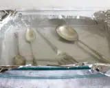 Srebrne sztućce w szklanej misce wyłożonej folią aluminiową.