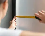 Precyzyjne pomiary to klucz do idealnych rolet dzień noc aranżacje. Dłoń z miarką przy oknie.