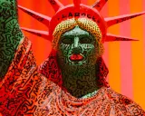 A vibrant Statue of Liberty sculpture, reimagined with Keith Haring's iconic political art style, features a green face with bold black lines and red lips, and an orange robe adorned with his signature figures.