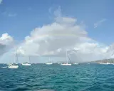 Un arc-en-ciel sur une mer bleue, parsemée de voiliers. L'appel de l'aventure : tout quitter pour vivre sur un bateau.