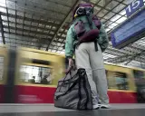 Traveler with backpack and duffel bag waits on a platform as a train speeds by.