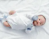 Dolce neonato nel suo primo mese, sdraiato su un soffice telo bianco, con calzini azzurri e guantini.