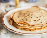 Una pila de masa crepes doradas y finas en un plato blanco.