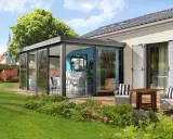 Moderne veranda sans permis de construire, avec table et chaises, offrant une vue sur un jardin verdoyant et des maisons.