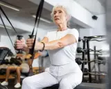 Starsza pani ćwiczy na siłowni, wykonując ćwiczenia na pelikany dla seniorów.