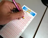 Ręka zaznacza liczby na kuponie Lotto, próbując wybrać szczęśliwe liczby.
