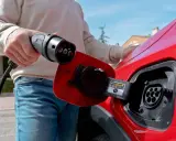 Persona desconectando el cargador de un coche eléctrico rojo.