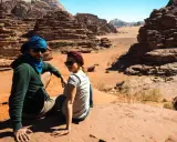 Para w turbanach odpoczywa na piasku, podziwiając skaliste krajobrazy pustyni Wadi Rum.