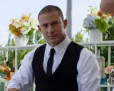 Channing Tatum som bartender i en film. Han ser ut att vara redo att servera drinkar med blommor och flaskor i bakgrunden.