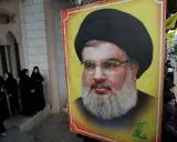 Wielki portret Hassana Nasrallaha, lidera Hezbollah, obok grupy kobiet w czarnych hidżabach.