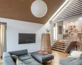 Modernes Wohnzimmer mit grauem Sofa und einem interessanten **split level** Design, das durch eine Holztreppe und einen offenen Wohnbereich gekennzeichnet ist.