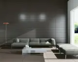 Nowoczesny salon z szarą kanapą i pufą. Zastanawiasz się, jakie płytki do salonu? Spójrz na te ciemne, eleganckie płytki na ścianie i jasne na podłodze.