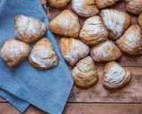 Sfogliatelle, un delizioso cibo tipico napoletano, cosparse di zucchero a velo su un tavolo di legno e un tovagliolo blu.