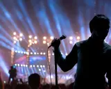 Cantante sul palco con microfono, luci sfocate e folla. Il **take on me significato** è l'essenza di un'esibizione che cattura l'anima.