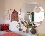 Stor rund spegel ger vardagsrum inspiration. En rutig jacka och tygkasse hänger på väggen.