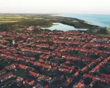 Luftaufnahme einer Küstenstadt in den Niederlanden mit roten Dächern, einem Leuchtturm und dem Meer. Drohnenaufnahmen zeigen die Schönheit der Niederlande.