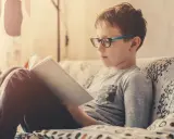 Bambino con occhiali legge un libro, concentrato su come imparare una poesia a memoria.