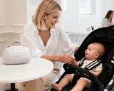Uśmiechnięta mama z niemowlakiem w wózku, przygotowująca się do sylwestra. Obok biała torba Momcozy.