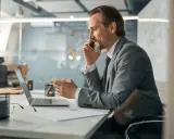 Mężczyzna w garniturze rozmawia przez telefon, pracując przy laptopie. To typowy dzień w pracy, nawet dla samego CEO.