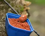 Niebieskie pudełko z zanętami Lorpio feeder, gotowe do akcji. Wędka w tle.