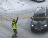 En räddningsarbetare spärrar av ett område med band. Snö faller och täcker marken och en bil. Kanske har något ruttnande material hittats.