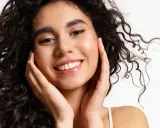 Sonrisa radiante con un toque de strawberry makeup, cabello rizado oscuro y piel luminosa.