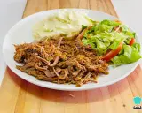 Plato de carne mechada jugosa, puré de papas cremoso y ensalada fresca de lechuga y tomate.