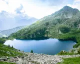 Un sereno lago ritorto incastonato tra montagne verdi e rocciose, con cime nebbiose all'orizzonte.