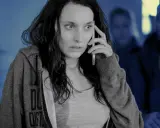 Przerażona kobieta rozmawia przez telefon, podczas gdy w tle widać zamazane postacie. Scena jak ze skandynawskich seriali kryminalnych.