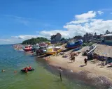 Słoneczny dzień na plaży, kolorowe łodzie na piasku, tłumy ludzi szukają idealnych miejsc na wakacje.