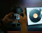Ręce trzymają smartfon, fotografując gramofon. Odkryj gadżety do domu, o których nie miałeś pojęcia, jak ten nowoczesny sposób na docenienie klasycznej muzyki.