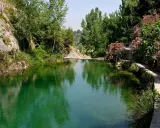Un remanso de agua verde rodeado de rocas y vegetación exuberante. Un camino serpentea junto al agua, ideal para explorar qué ver en Ontinyent.