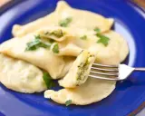 Pyszne pierogi ze szpinakiem i serem feta, udekorowane natką pietruszki, czekają na widelcu.