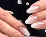 Dłonie z paznokciami w stylu french z pyłkiem, delikatny ombre od różu do bieli, subtelny blask.