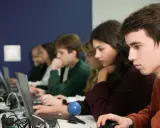 Studenci podczas zajęć z informatyki w Katowicach, skupieni na ekranach laptopów.