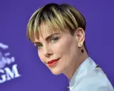 Charlize Theron mit fransigen Kurzhaarfrisuren Damen, rotem Lippenstift und Stern-Herz-Ohrringen vor MGM-Logo.