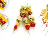 Brochetas de frutas coloridas con fresas, kiwi, plátano, mango, naranja, uvas y nueces. ¡Un postre refrescante y saludable!