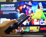 Dłoń trzymająca pilot do telewizora, na ekranie menu platformy streamingowej. Wady i zalety reklamy telewizyjnej – czy warto ją oglądać?