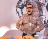 Popek kiedys, wytatuowany mężczyzna w okularach przeciwsłonecznych, z złotym łańcuchem i wisiorem, napina mięśnie.