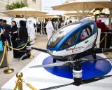 Ein futuristisches Flugtaxi, ein Dubai Drohne, steht auf einer Ausstellungsplattform. Menschen in traditioneller Kleidung betrachten das Gefährt.